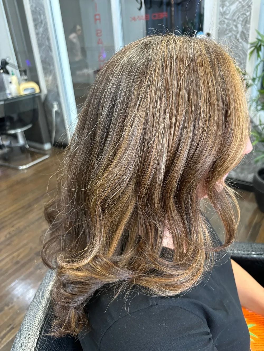 Side view of a woman’s wavy brown hair with blonde highlights in a salon chair