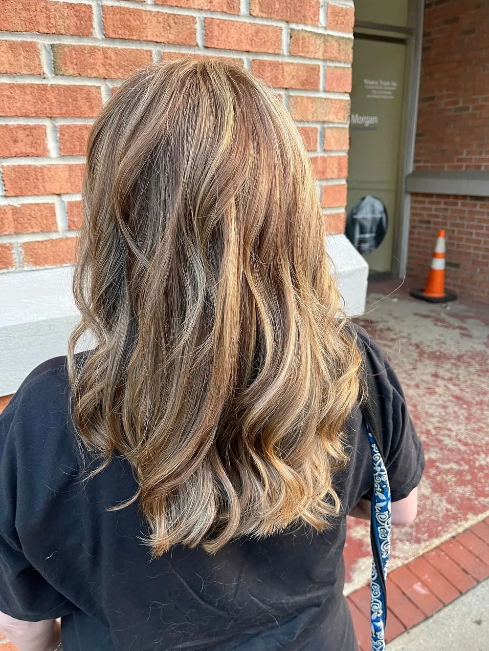 Back view of a person with wavy brown hair standing by a brick building entrance