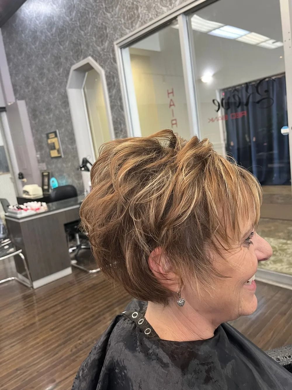 Short layered haircut with blonde highlights in a salon, shown in side profile.