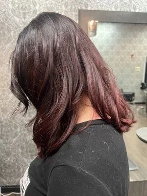 Back view of a person with shoulder-length dark hair in a black top, standing indoors near a mirror.