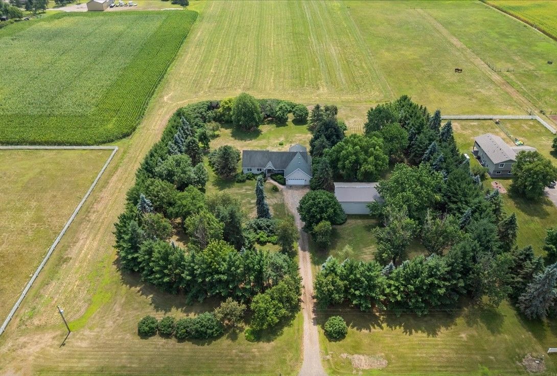 Aerial view of a farmhouse surrounded by dense trees and fields with a long dirt driveway.