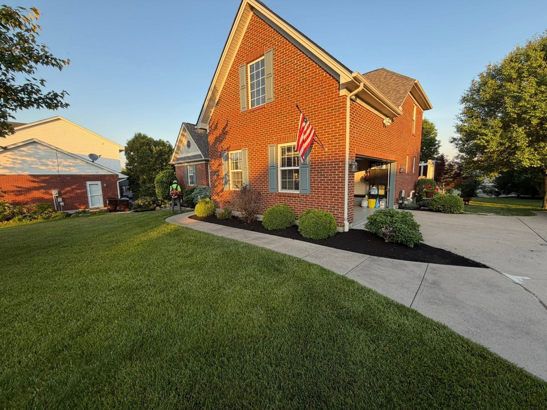 Orange two-story house with white trim, green lawn, and curved driveway at sunset
