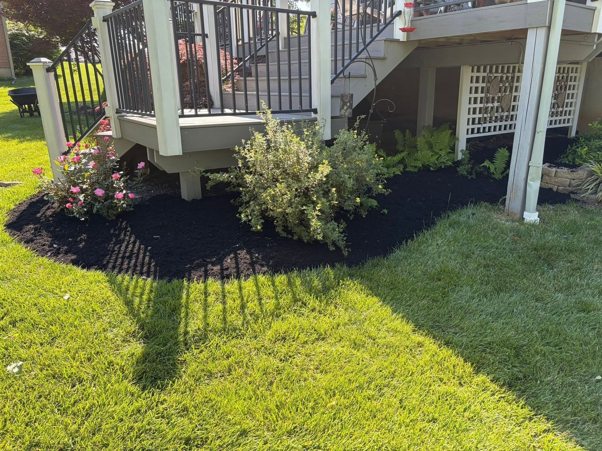 Front porch with white railings, black mulch bed, and green lawn in bright sunlight