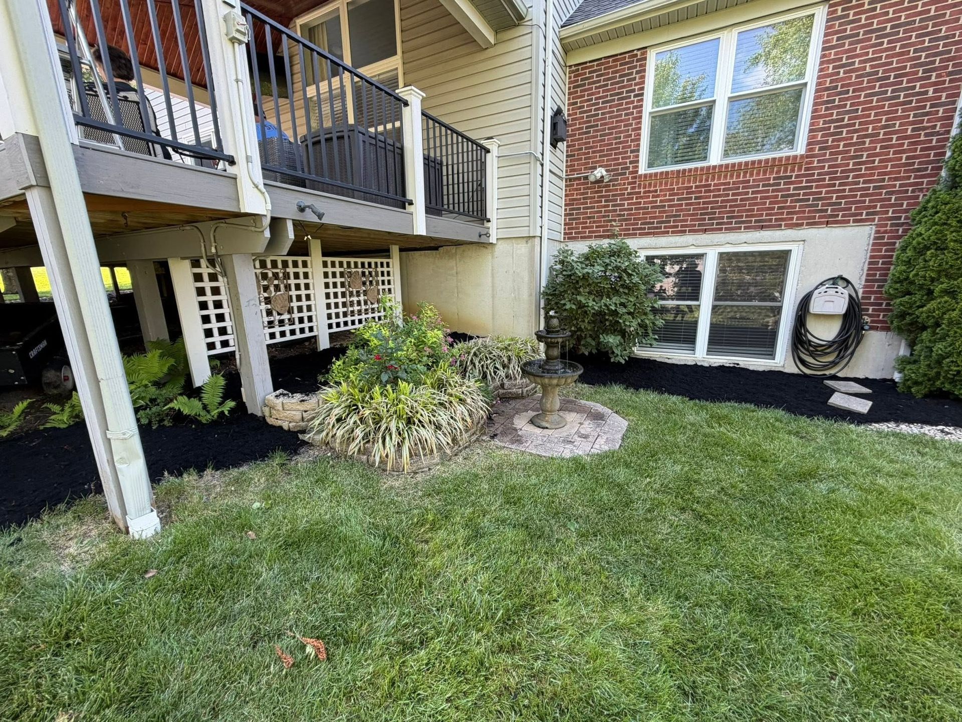 Apartment courtyard with green lawn, shrubs, brick wall, and balcony above