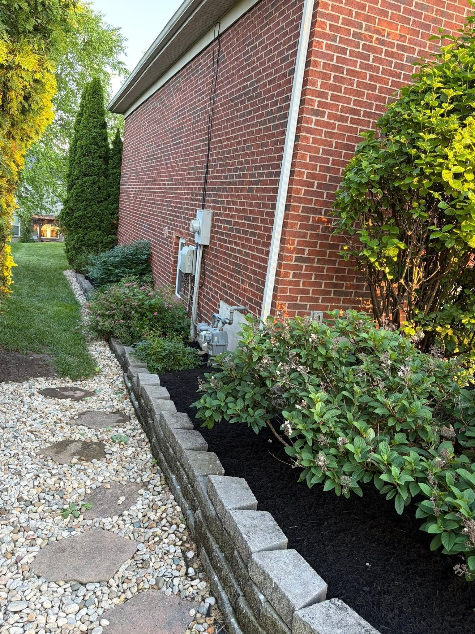 Brick house side yard with stone path, white utility boxes, shrubs, and landscaped gravel border