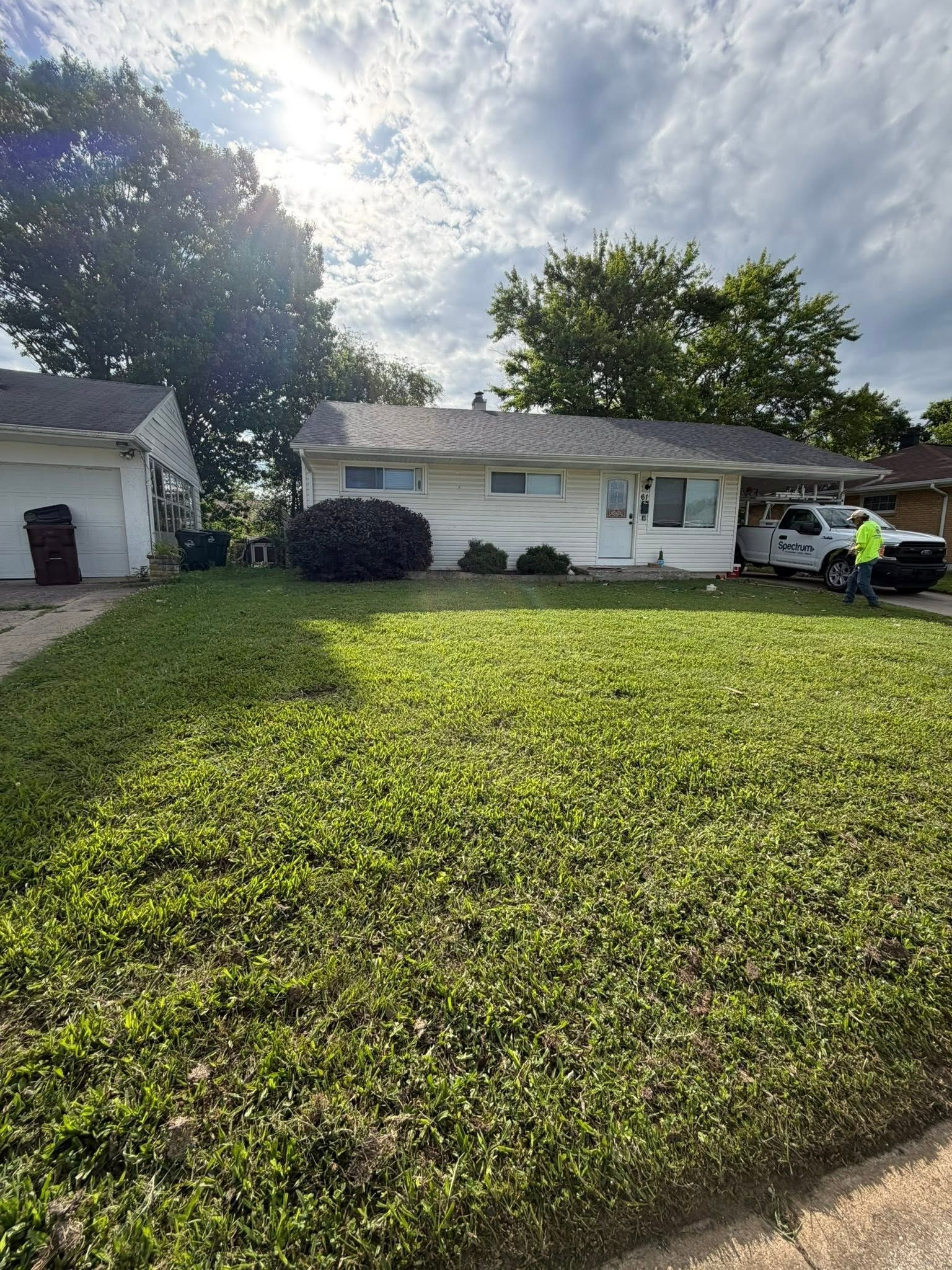 Single-story white house with a green lawn, driveway, and parked car under a bright sun.