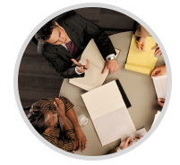 Overhead view of three people collaborating around a table with papers and notebooks