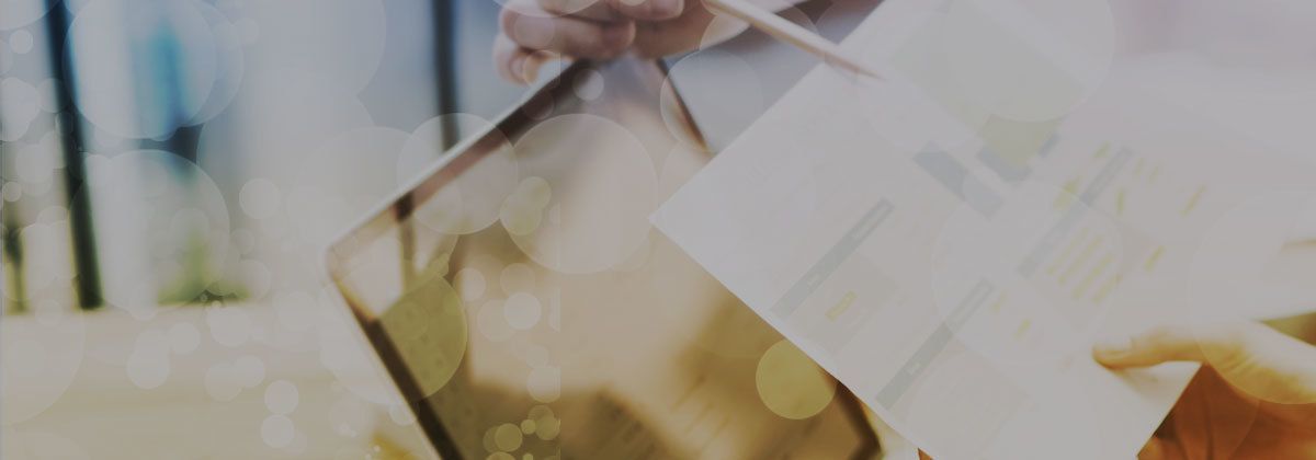 Blurred close-up of white papers and a gold-toned glass object on a desk, with bright window light.