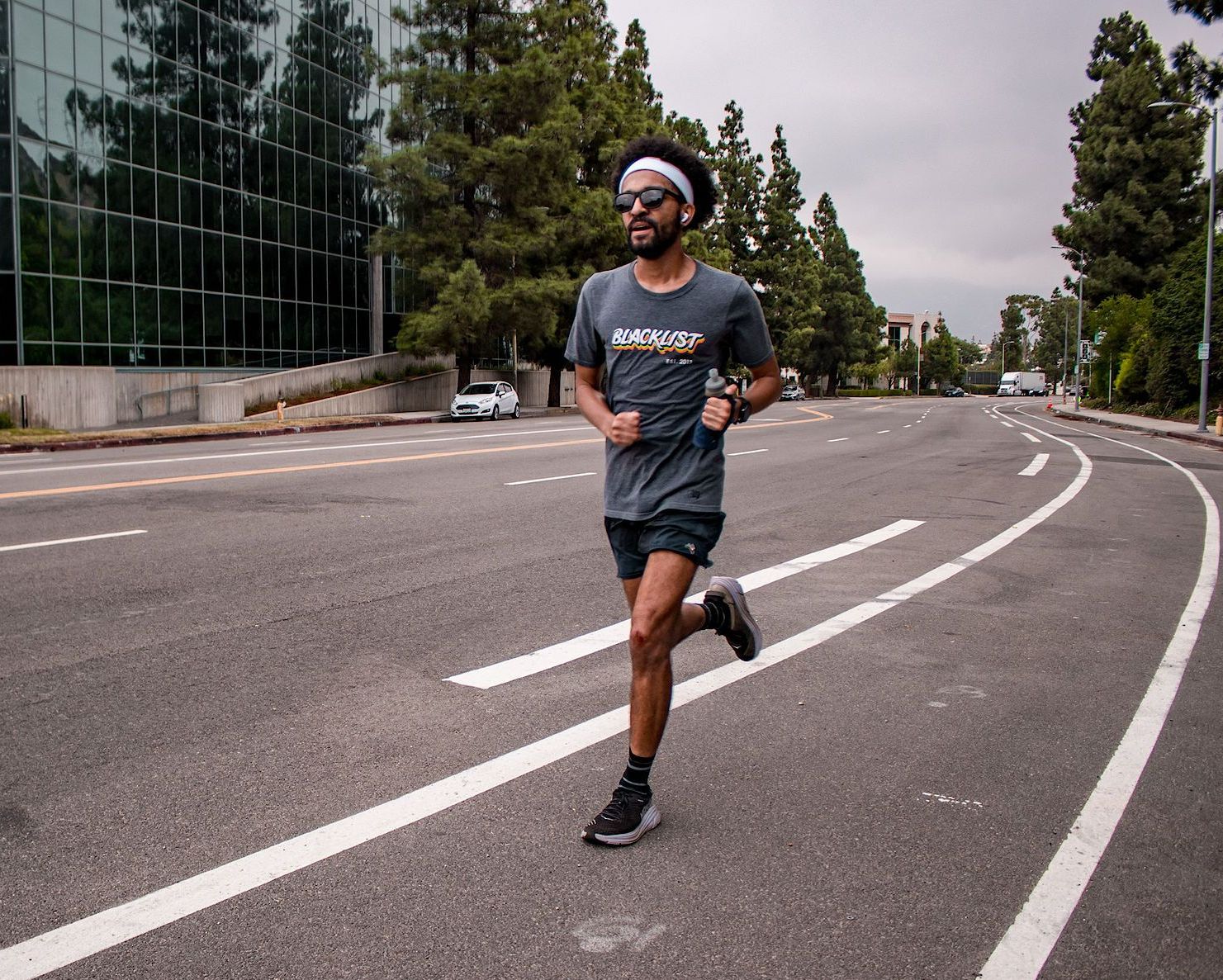 A man wearing sunglasses and a headband is running down a street.