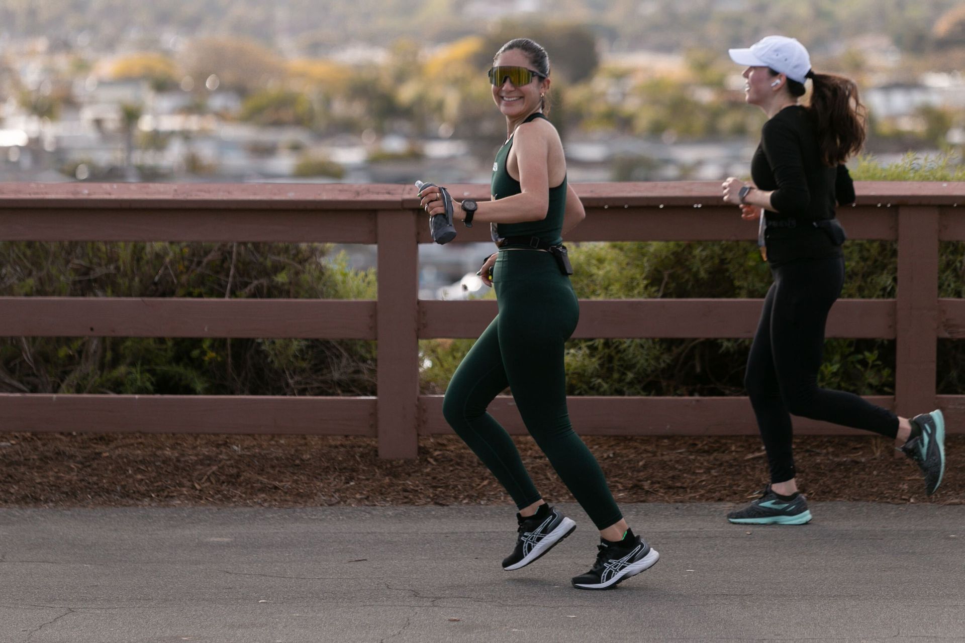 Two women are running on a path next to a fence.
