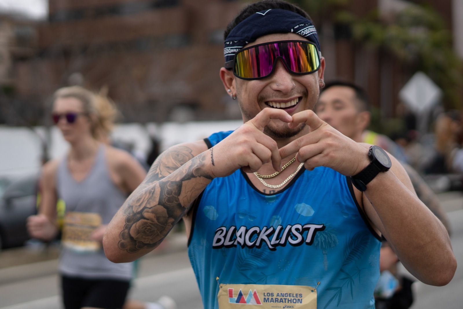 A man wearing sunglasses and a blacklist shirt is making a heart shape with his hands.