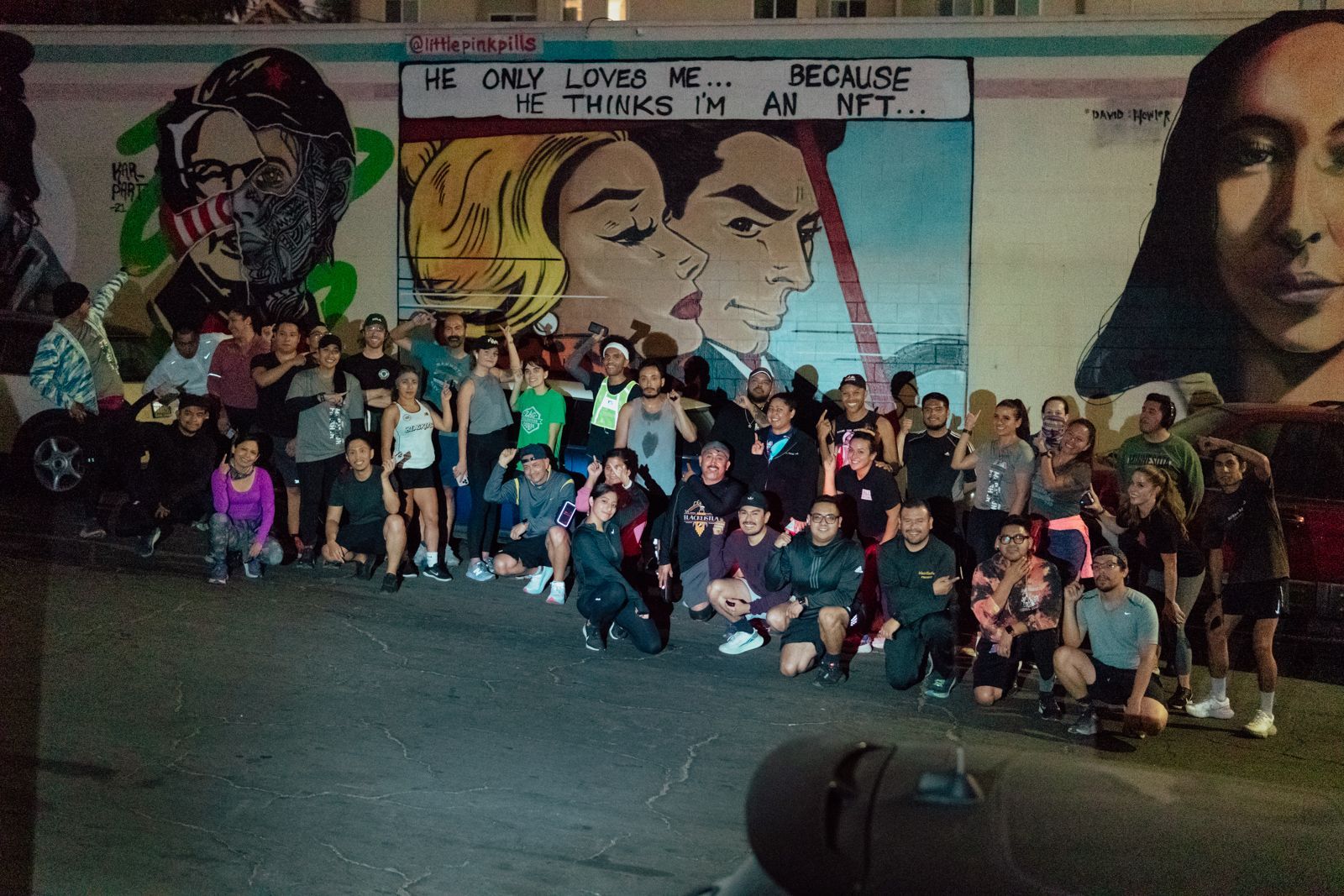 A group of people posing in front of a mural that says he only loves me