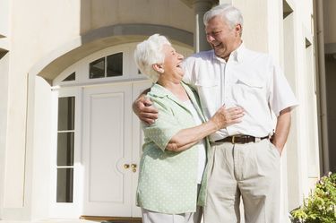 Two people smiling and hugging while standing in front of the white door of a building.