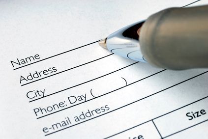 A close-up view of a pen hovering over a blank form with fields for name, address, city, phone number, and email address.