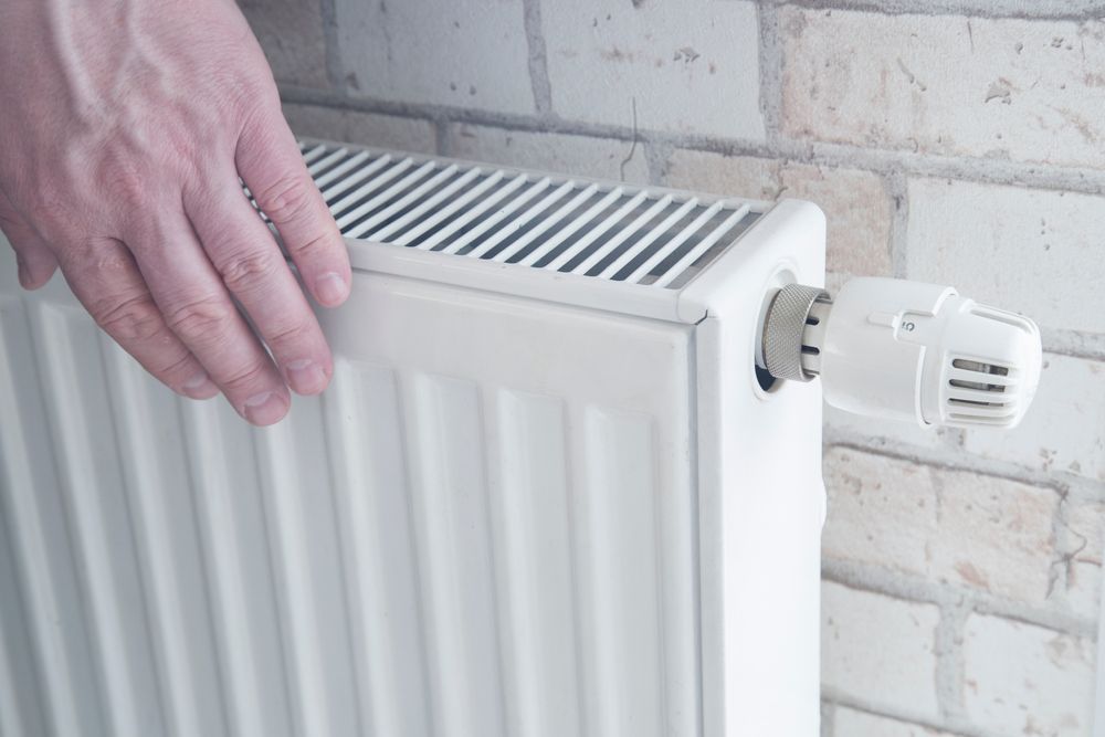 Vérification manuelle d'un radiateur blanc muni d'un robinet thermostatique sur un mur de briques