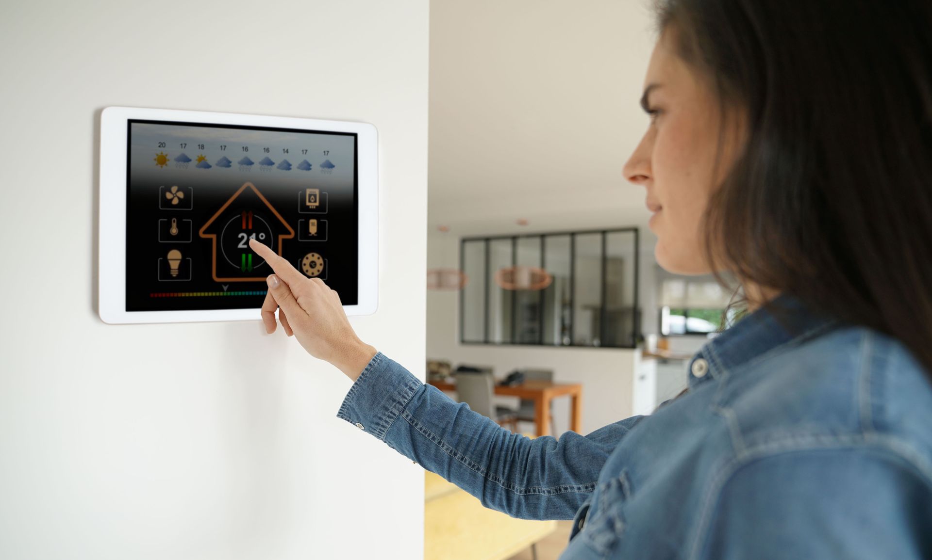 Femme utilisant un panneau de commande domotique tactile fixé au mur à l'intérieur.