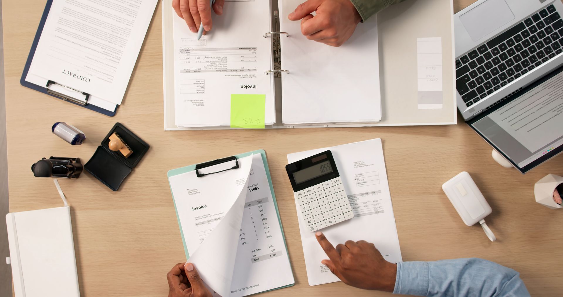 Overhead view of a business meeting with papers, calculator, laptop, and hands reviewing documents