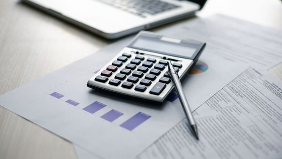 Calculator and pen on financial documents with a laptop in the background