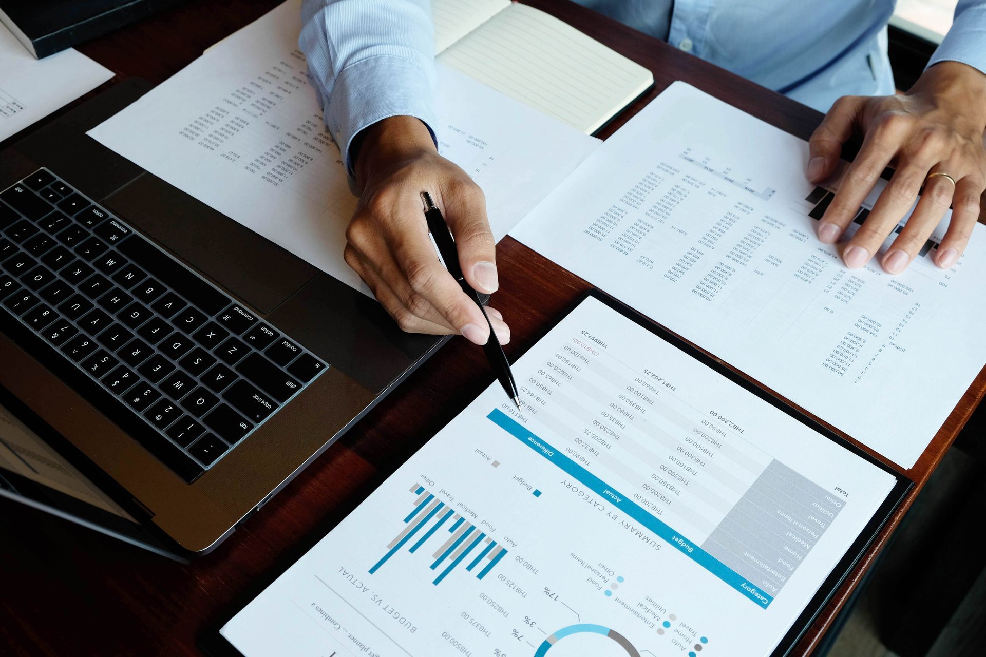 Hands reviewing printed charts and reports beside a laptop on a desk