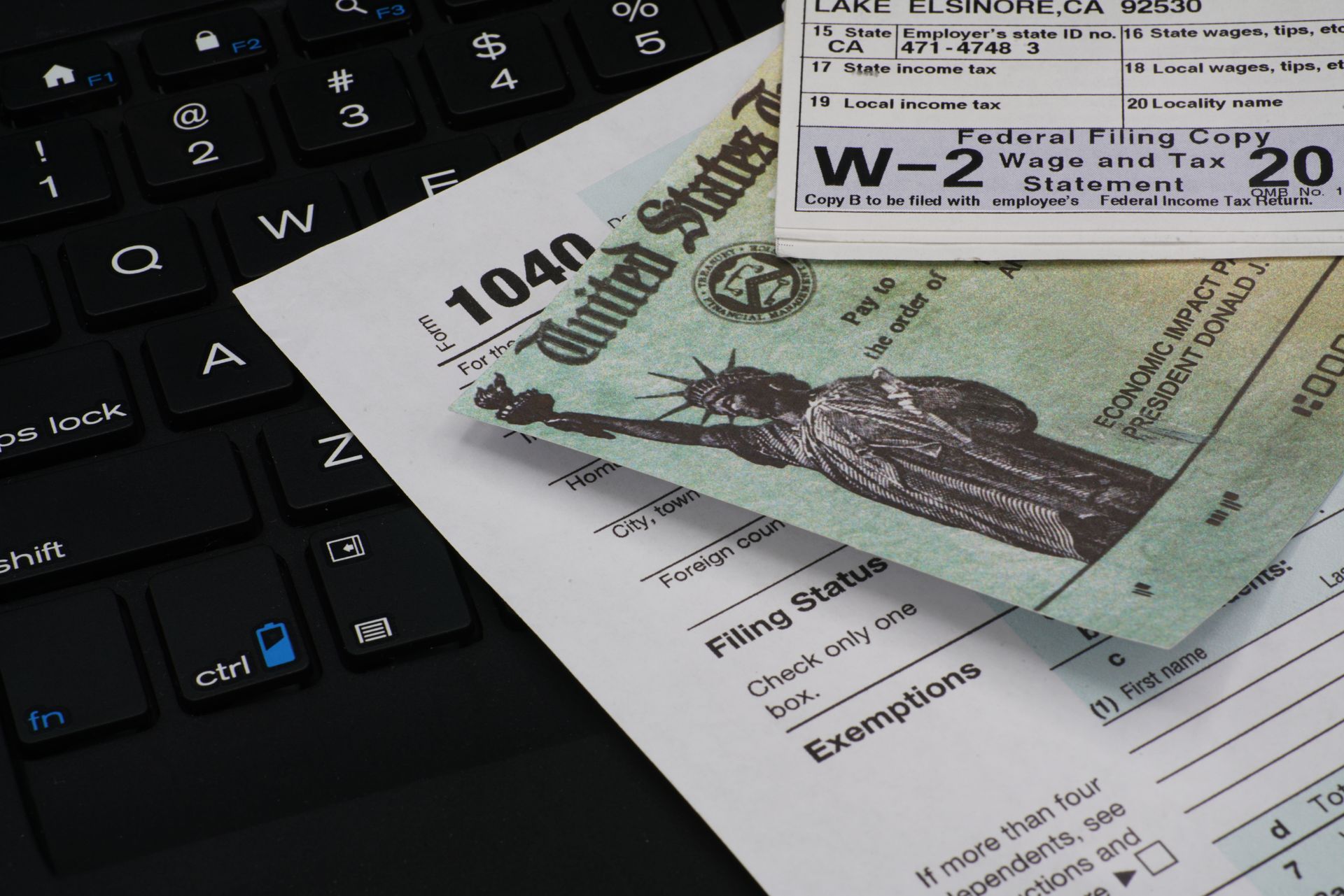 Tax forms, cash, and a W-2 form on a laptop keyboard