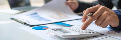 Hands using a calculator beside printed financial charts on a desk
