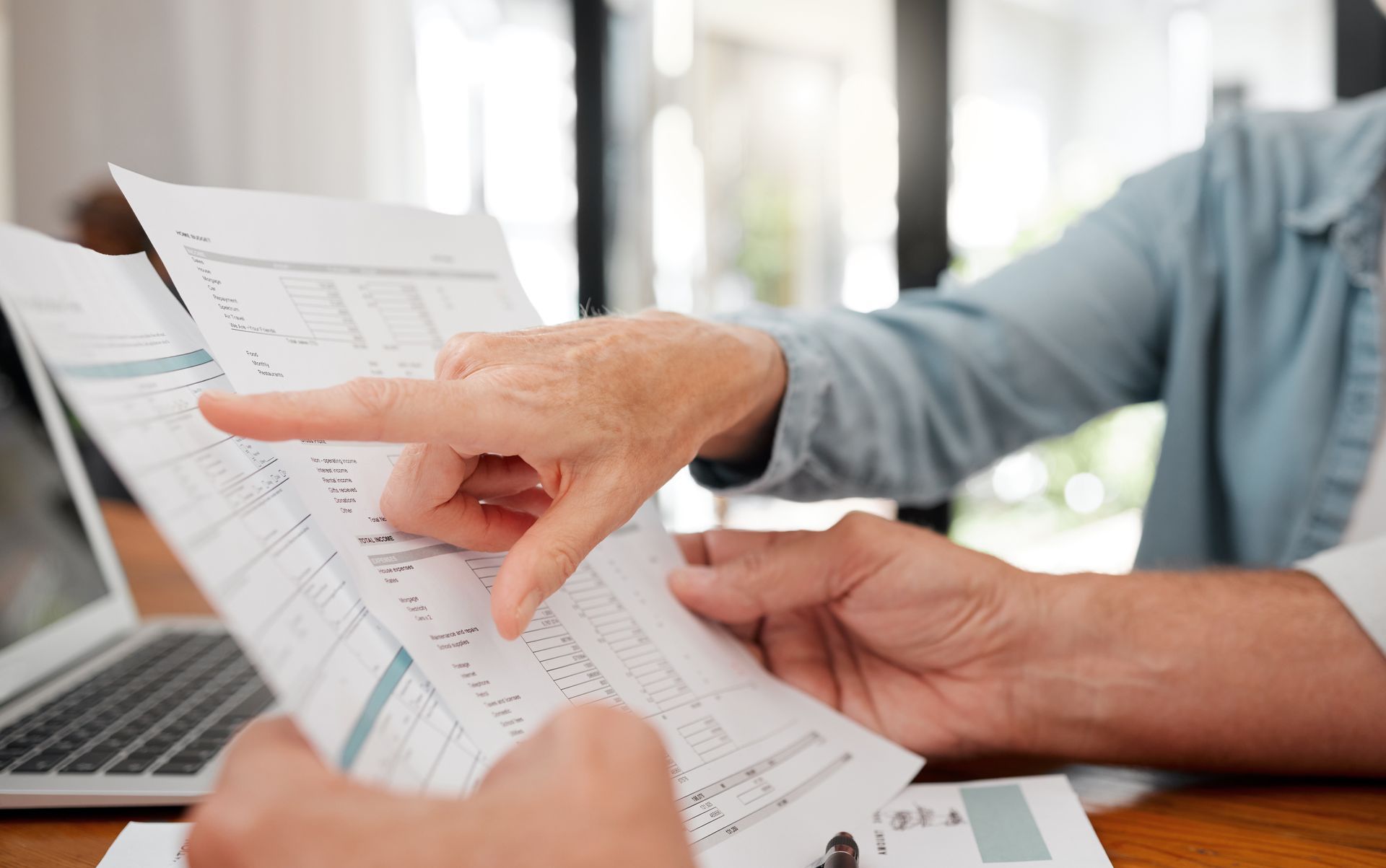 Hands pointing at printed charts beside a laptop in a bright office workspace