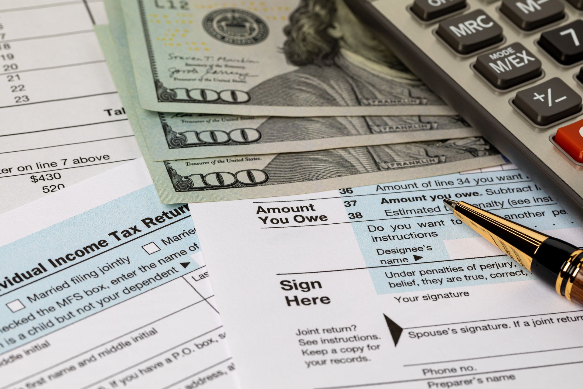 Tax forms, cash, calculator, and pen on a desk for financial planning and filing.