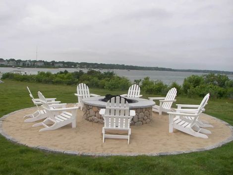 a fire pit surrounded by white chairs with a view of the ocean