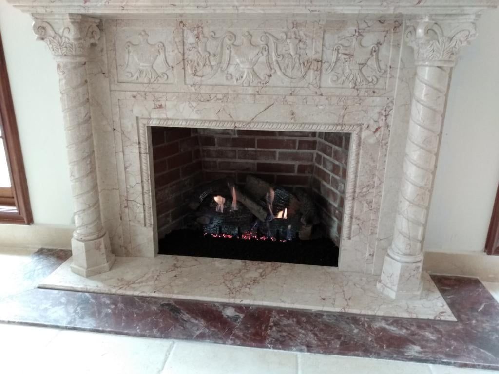 A fireplace with a marble mantle and a brick surround is lit up in a living room.