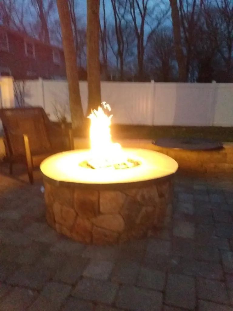 A fire pit is lit up at night on a patio.