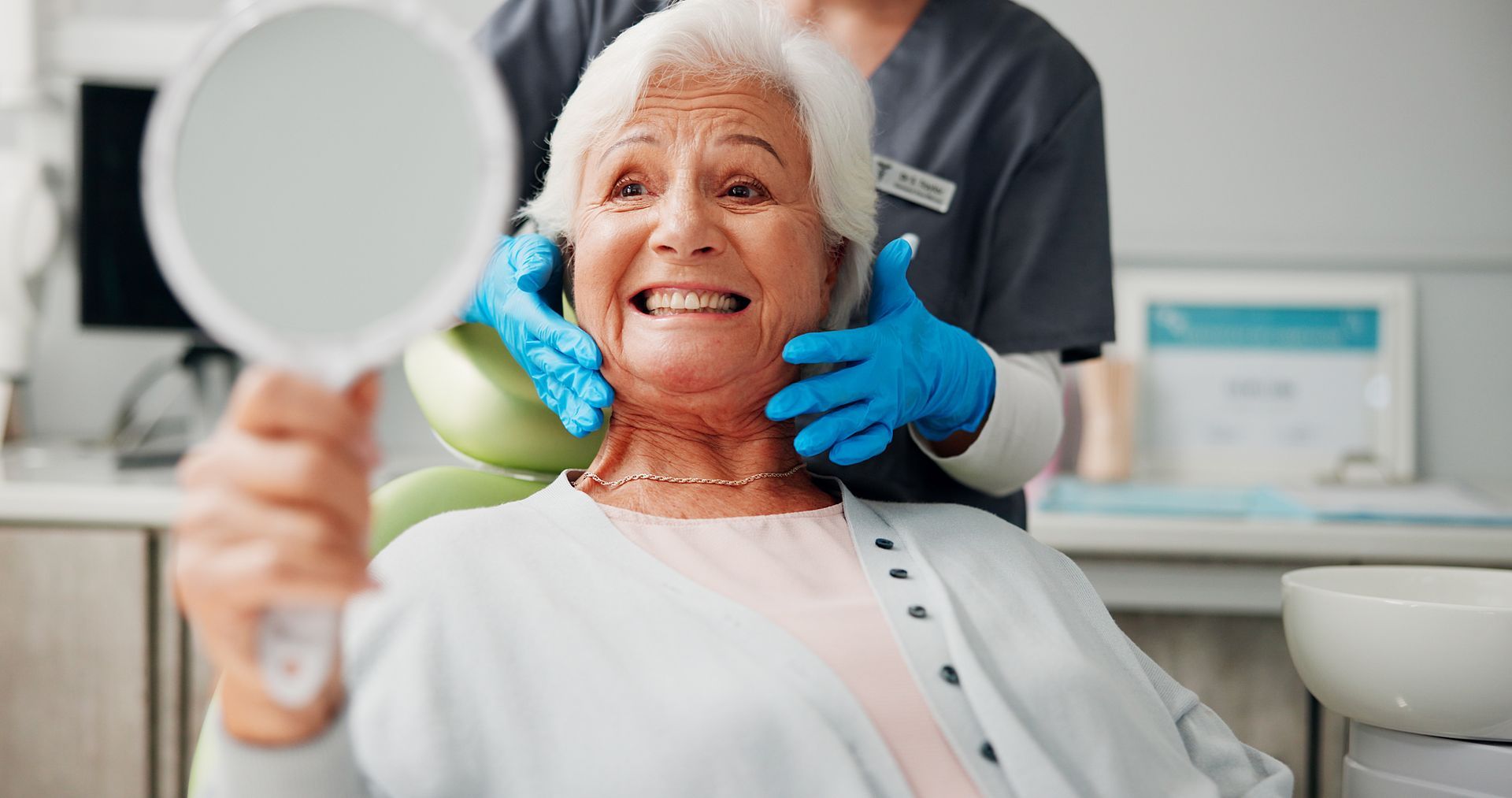 Dentist holding a mirror while examining a smiling patient in a dental chair.