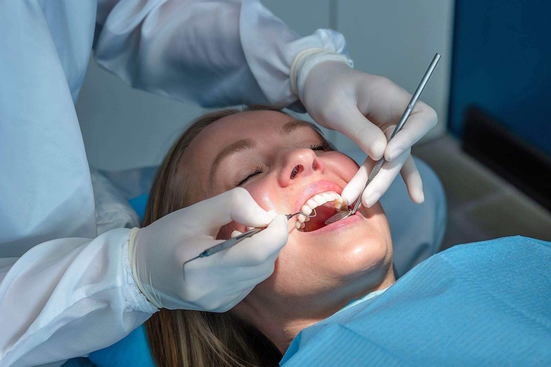 Dentist examining a patient’s mouth with gloved hands and dental tools in a clinic.
