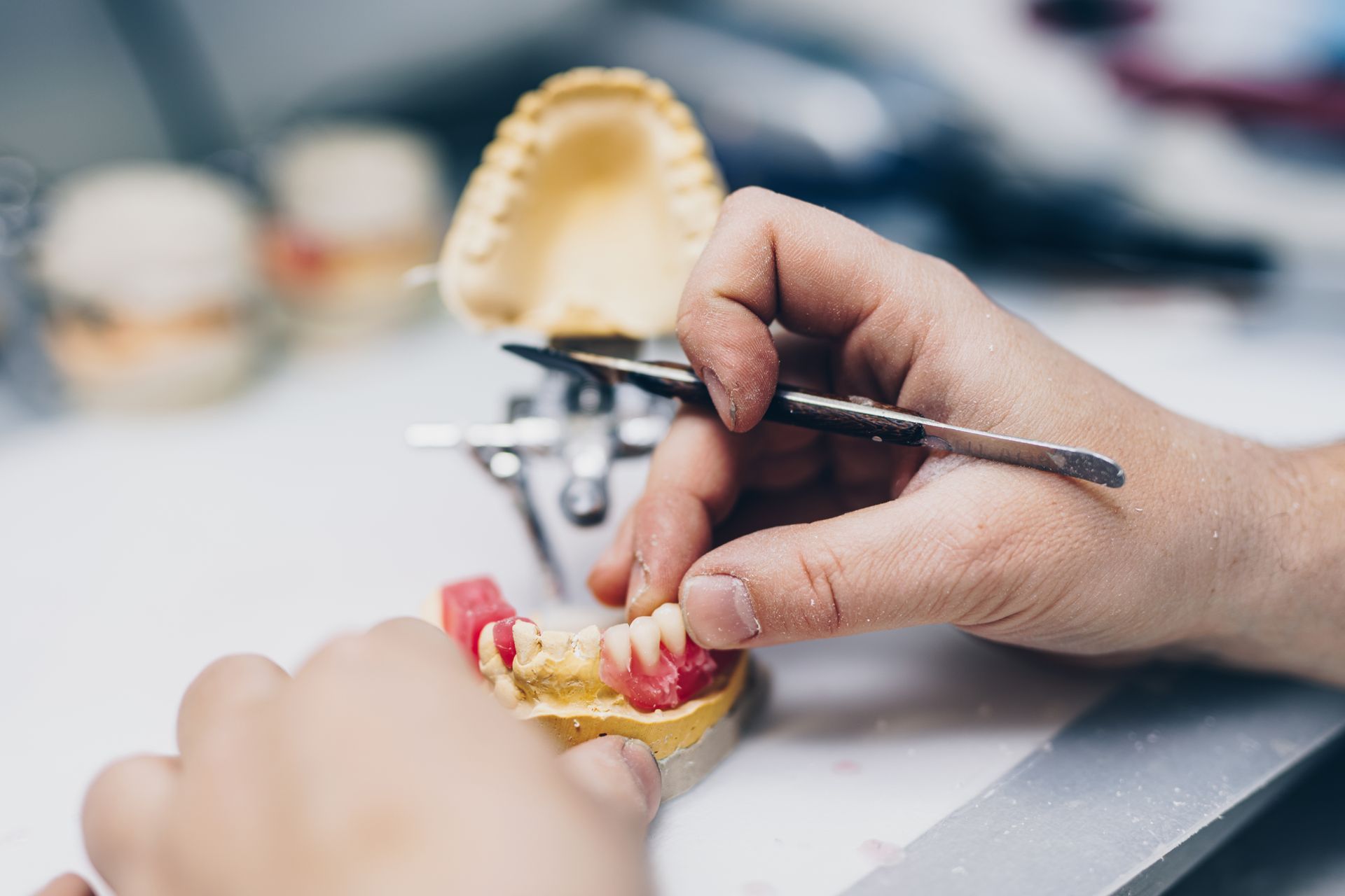 Hands shaping a dental mold with pink and yellow dental impressions on a workbench.