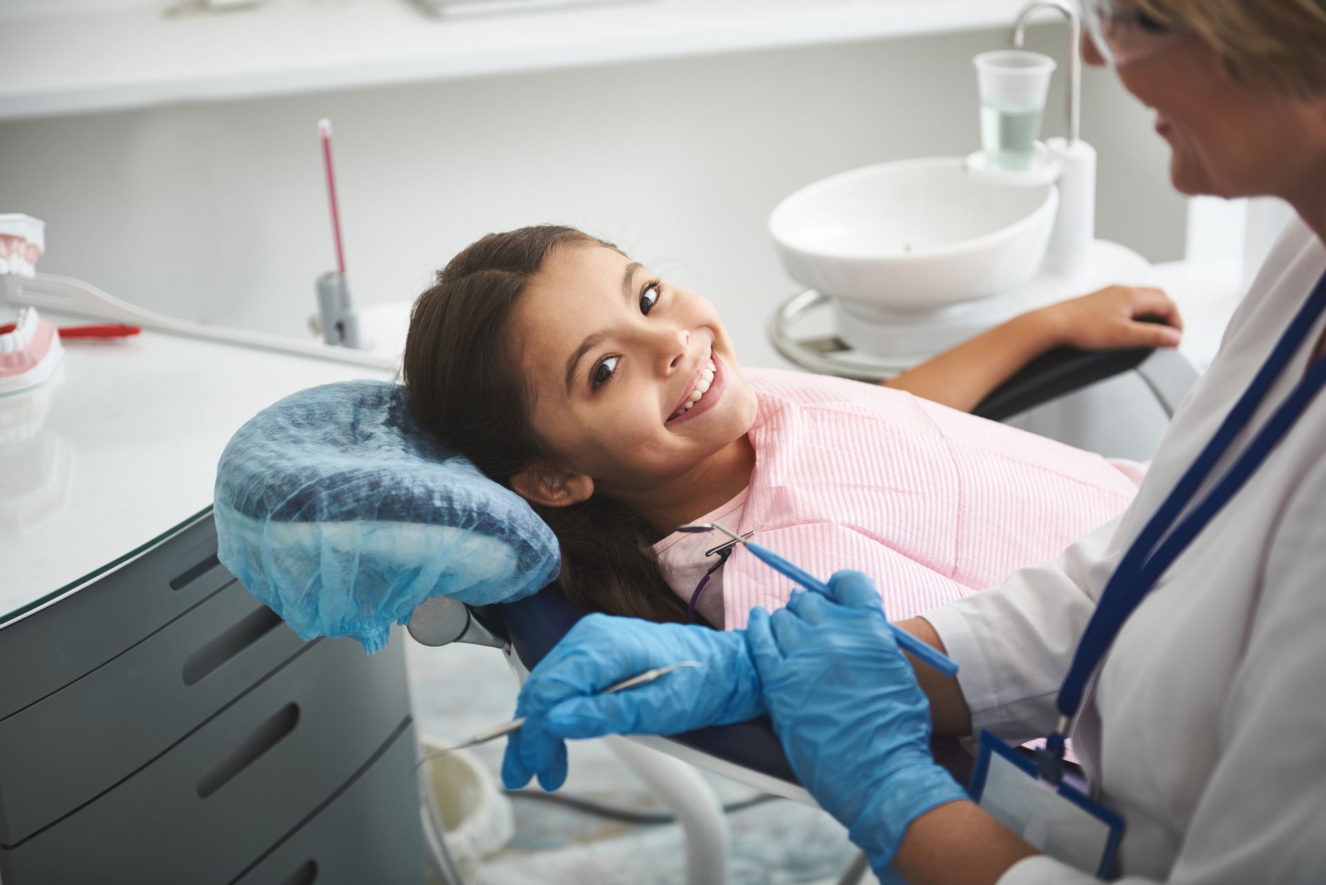 Dentist treating a smiling child in a dental chair, with blue gloves and dental tools visible.