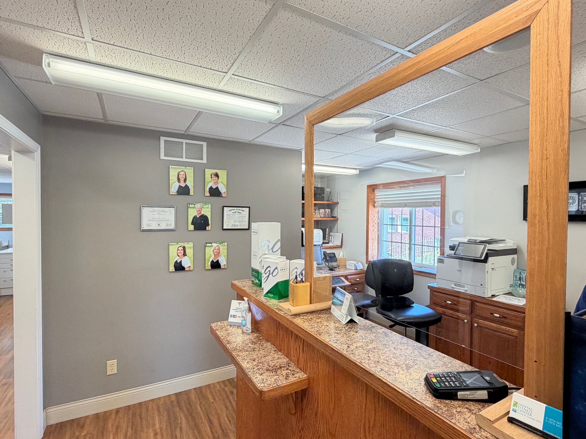 Small office reception area with wood counter, gray walls, office chair, and wall photos