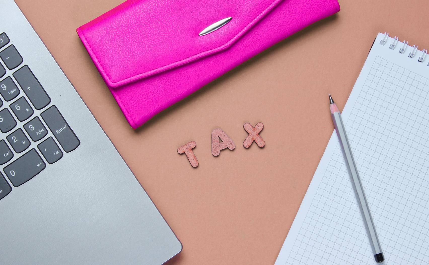 Desk with laptop, pink pencil case, TAX letters, pencil, and notepad on a peach background.