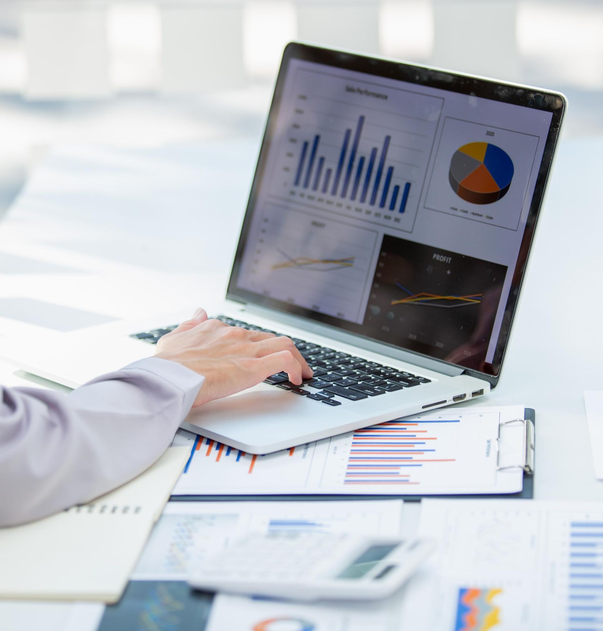 Person working on a laptop with sales charts and graphs on screen in a bright office