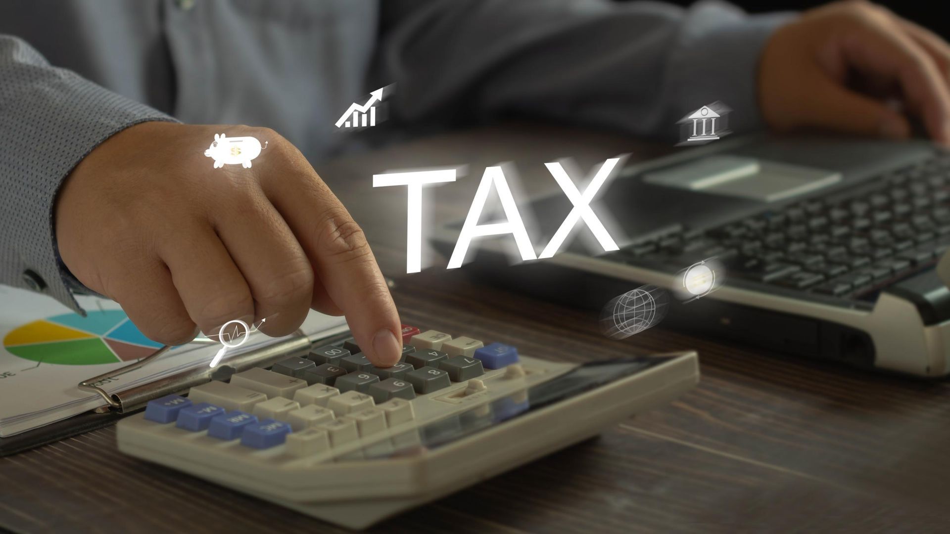 Hand using a calculator beside a laptop and tax paperwork with “TAX” text overlay