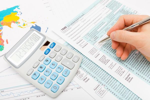 Hand calculating taxes on a form with a calculator and pen, with charts in the background