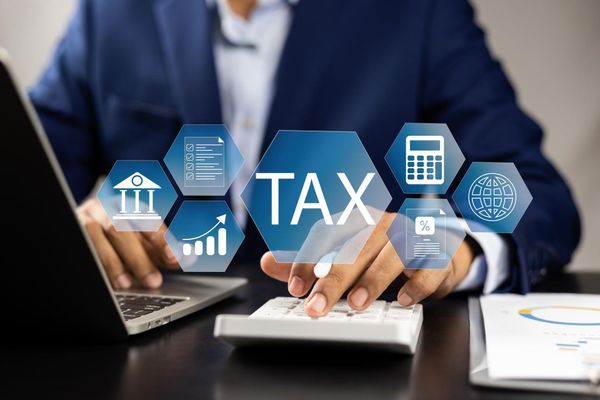 Businessperson typing on a laptop beside a calculator with “TAX” icons on a desk.