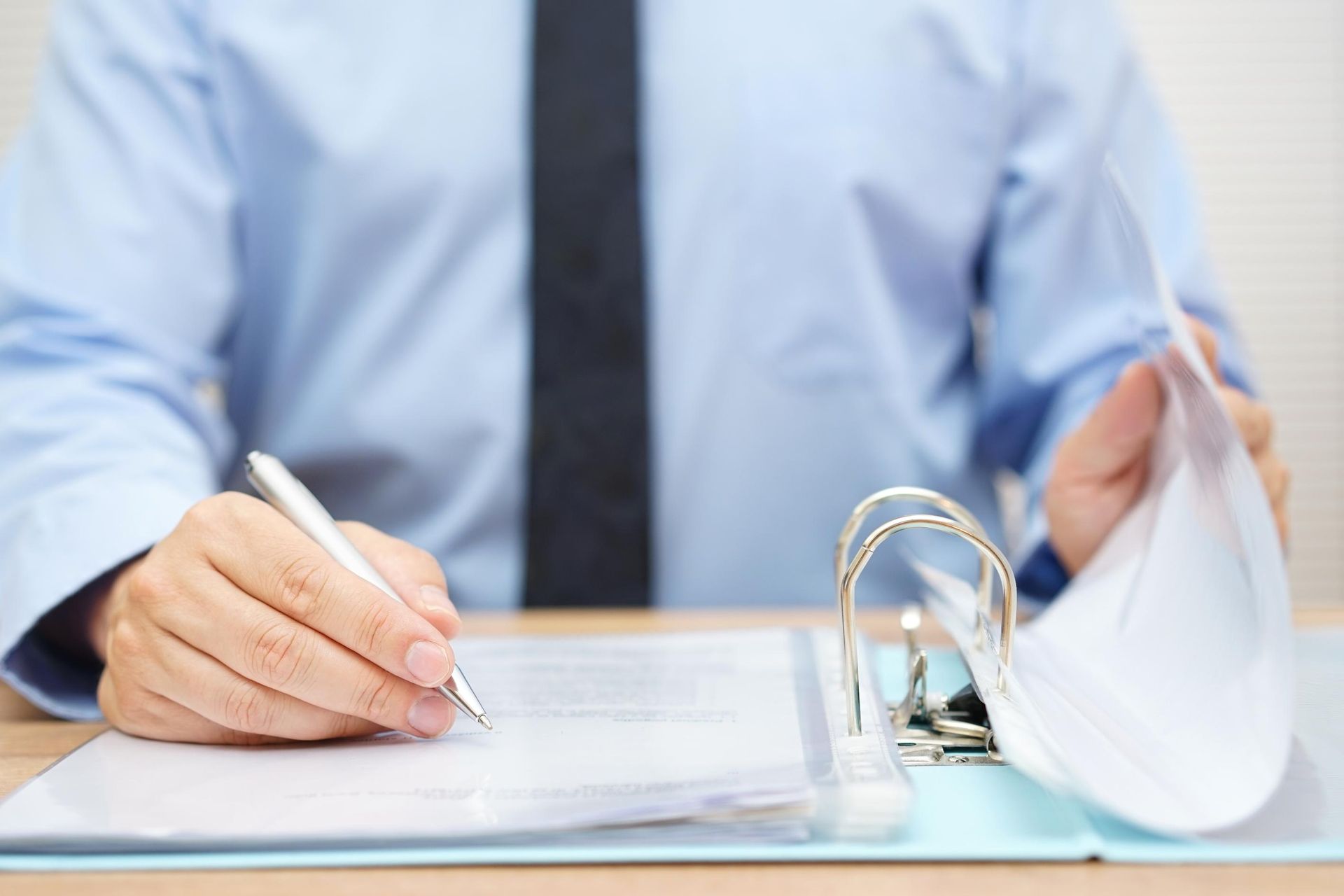 Person signing documents at a desk beside a binder and face mask