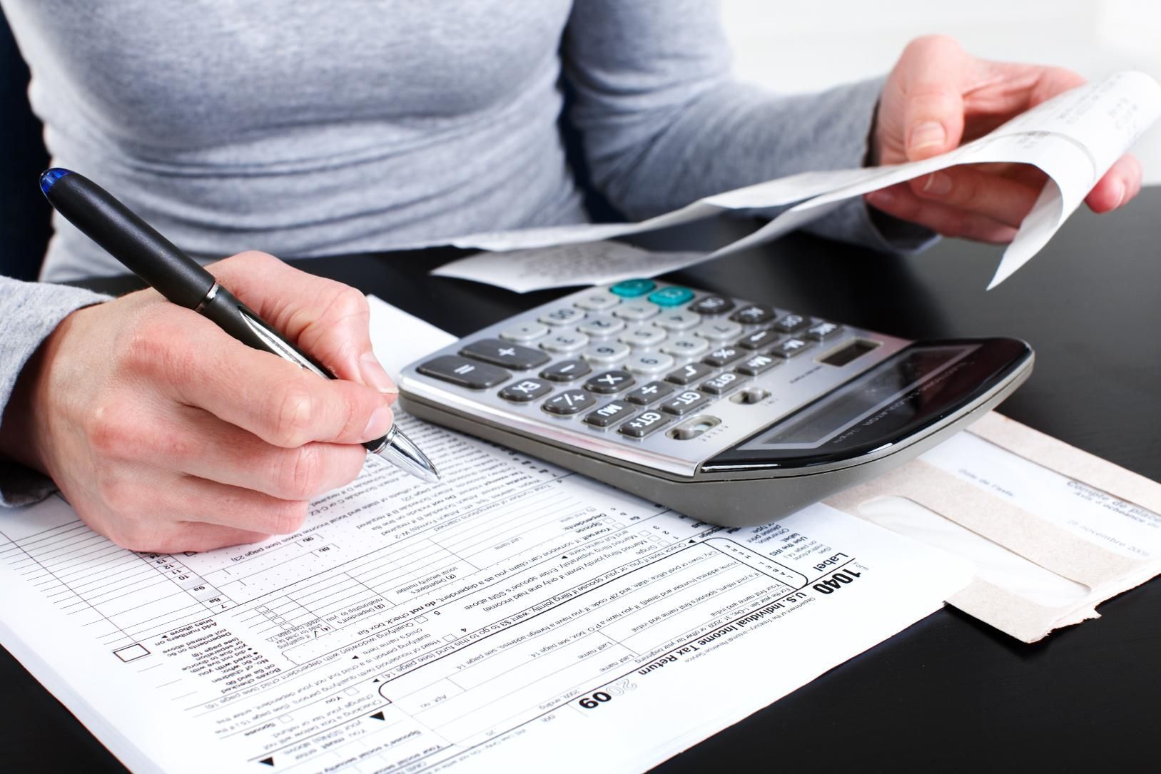 Hands using a calculator and pen on financial documents at a desk