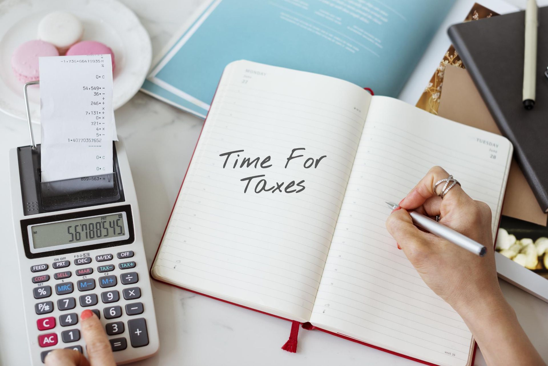Calculator, tax receipt, and notebook reading “Time For Taxes” beside a hand writing on a desk.