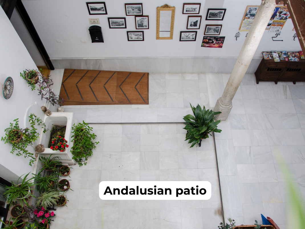 Bright Andalusian patio with white walls, potted plants, tiled floor, and wooden bench seating