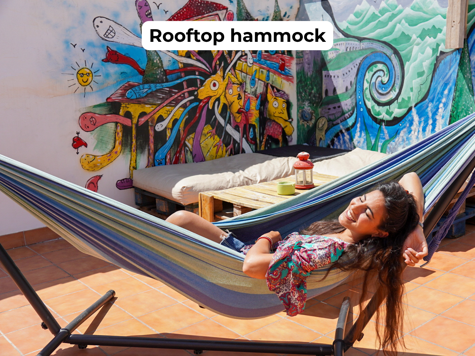 Woman relaxing in a striped rooftop hammock beside a colorful mural.