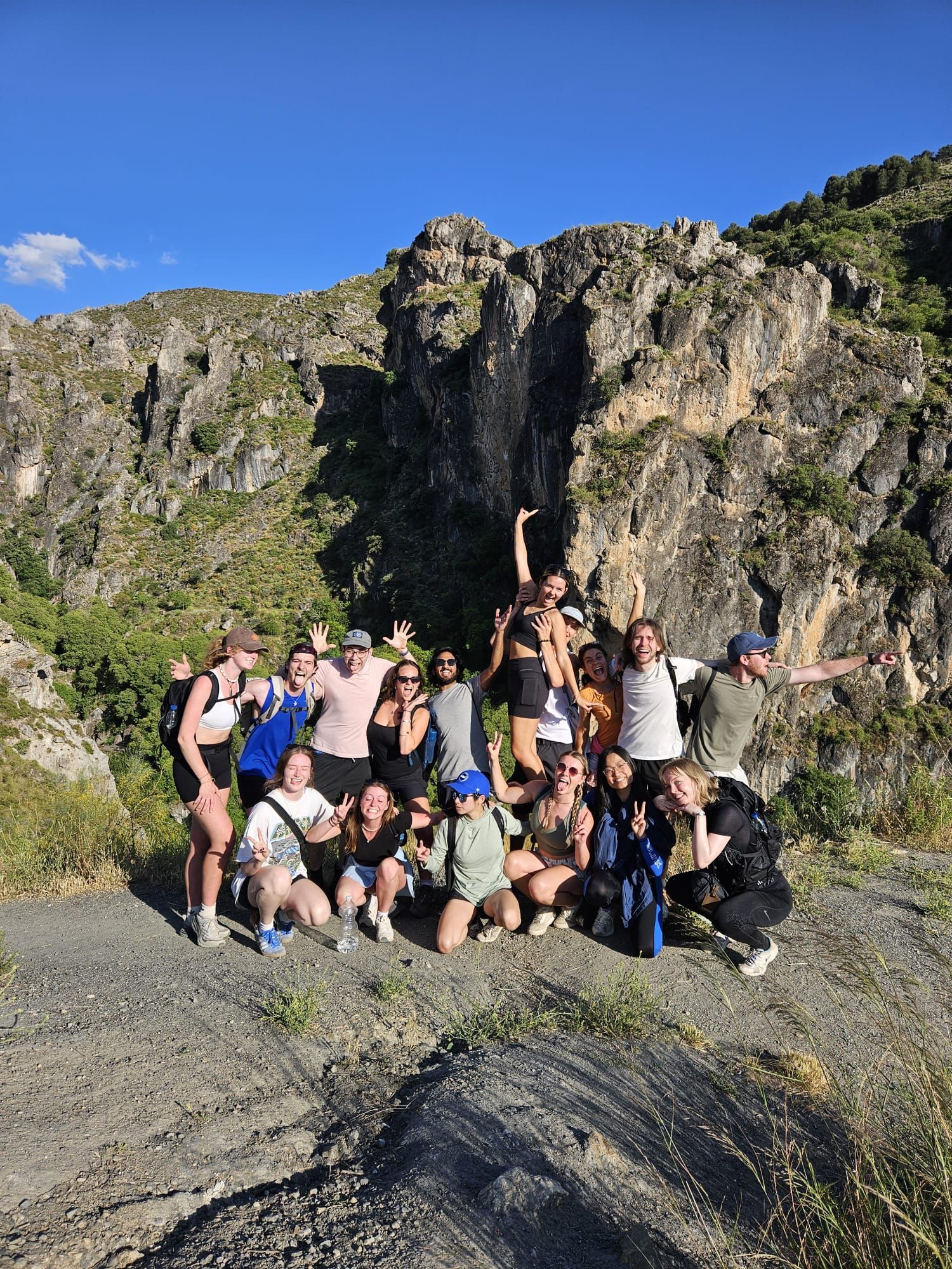 Group of hikers posing on a rocky trail with cliffs and blue sky in the background
