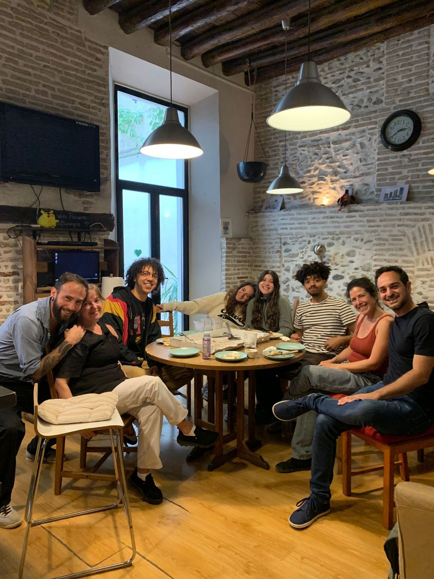 Group of people chatting around a table in a cozy brick-walled café with hanging lights.