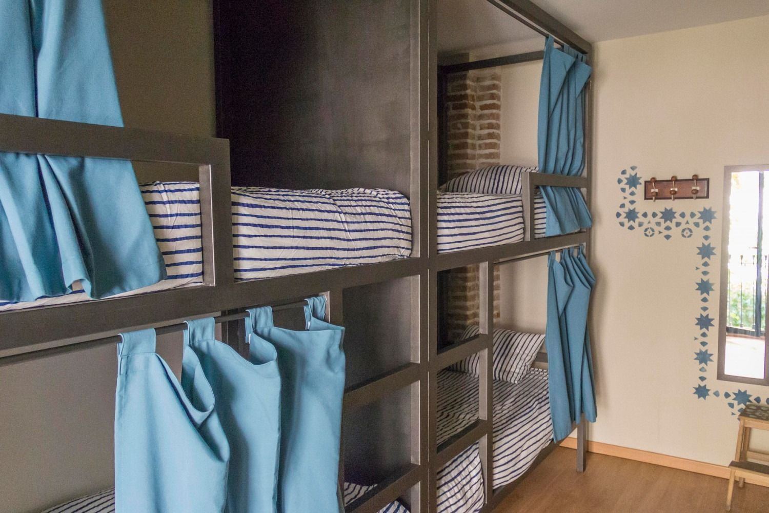 Bunk beds with blue curtains and folded linens, in a 6 bed dormitory room.