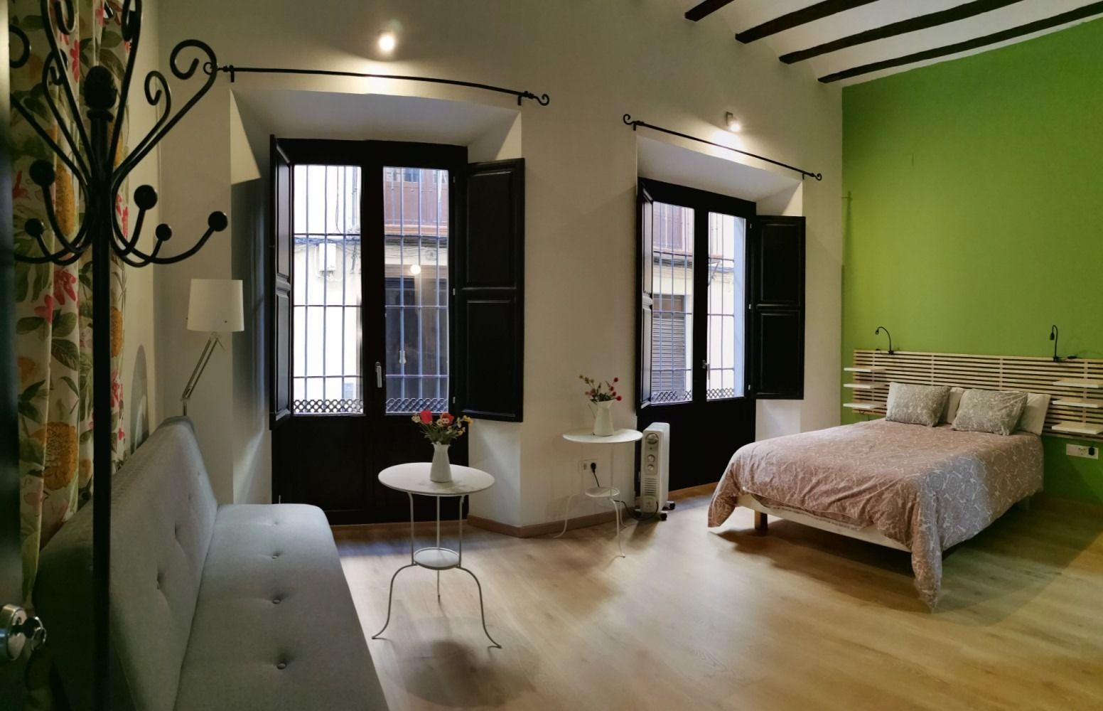 Bright modern bedroom with green accent wall, black doors, bed, sofa, and small table near tall windows