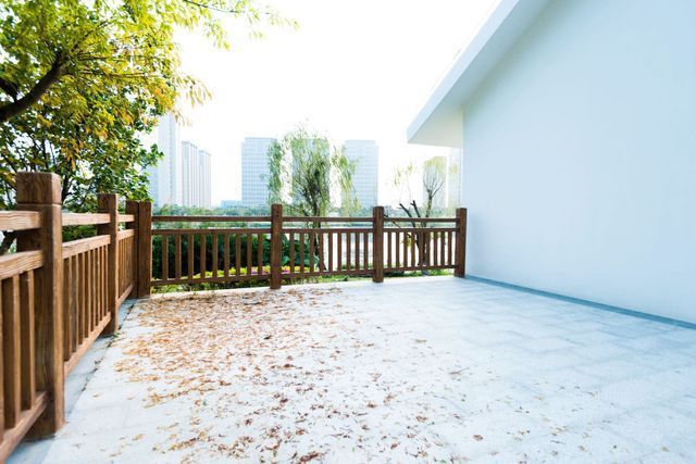 An empty patio with a wooden fence and leaves on the ground.